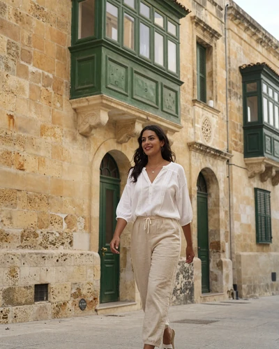 Maltese woman walking through the golden limestone streets of Valletta with traditional green balcony above